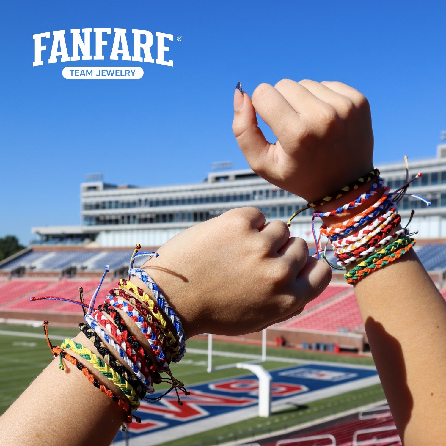 Two hands wearing colorful braided bracelets with a stadium in the background, featuring the Fanfare Team Jewelry logo.